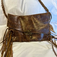 a brown leather purse with tassels on the front and shoulder strap, sitting on a white sheet