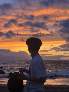 a man standing on top of a beach next to the ocean under a cloudy sky