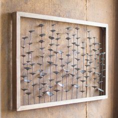 a wooden frame with metal flowers in it on the wall next to a brick wall