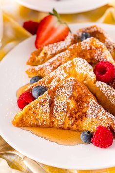 three pieces of french toast on a plate with berries and powdered sugar next to it