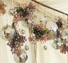 several disco balls hanging from the ceiling with flowers and greenery in them on display