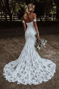 a woman in a white wedding dress is standing outside with her back to the camera