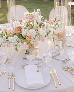 the table is set with white plates and silverware, gold cutlery, and flowers in vases