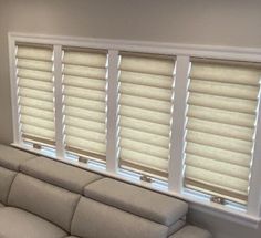 a white couch sitting under three windows in a living room next to a window with blinds on it