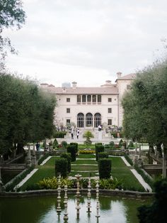 a large white building sitting next to a lush green park filled with lots of trees