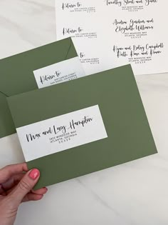 two green envelopes with white paper on them and one being held by a woman's hand