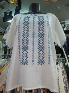 a white shirt with blue and orange designs on it's chest, sitting on a mannequin