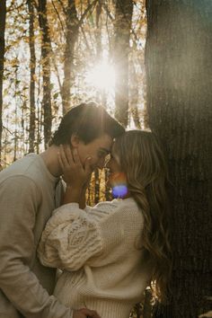 a man and woman standing next to each other in the woods with sunlight shining down on them