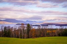 a scenic view of the mountains and water from a grassy field with trees in the foreground