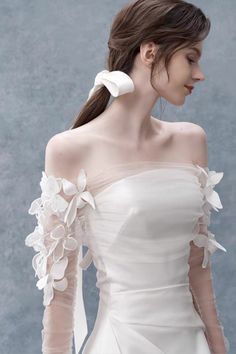 a woman in a white dress with long sleeves and flowers on her shoulder is looking down