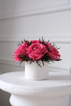 a white vase filled with pink flowers sitting on top of a white table next to a wall