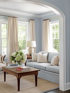 a living room filled with furniture and windows covered in drapes on top of them