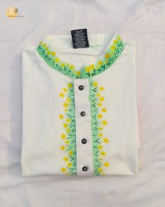 a white shirt with yellow and green flowers on the front, along with black buttons