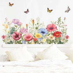 a bed with white sheets and pillows in front of a flowered wall decal