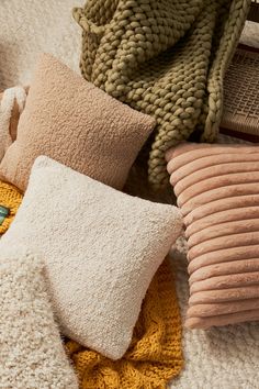 several pillows and blankets on the floor with knitted throws around them, all in different colors