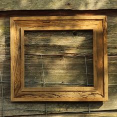 a wooden frame hanging on the side of a fence with barbed wire around it and a wood wall behind it