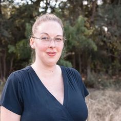 a woman wearing glasses standing in front of trees