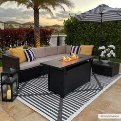 an outdoor fire pit on a patio with black and white striped rug, palm trees, and potted plants