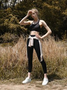 a woman in black and white sports bra top standing on the ground with her hands behind her head