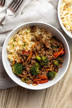 two bowls filled with rice, meat and vegetables on top of a table next to a fork