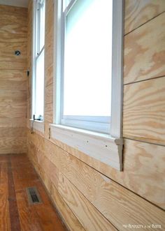 an empty room with wood paneling on the walls and wooden floors in front of a window