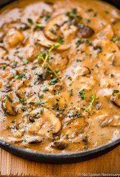 a skillet filled with mushrooms and gravy on top of a wooden table