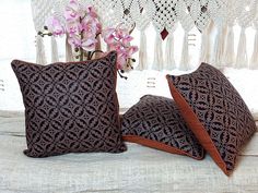 two decorative pillows sitting on top of a bed next to a vase with flowers in it