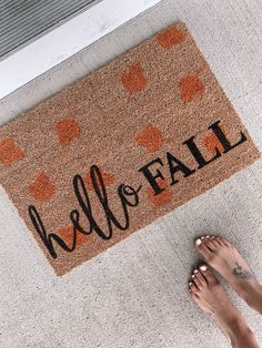 a person standing in front of a door mat that says hello fall