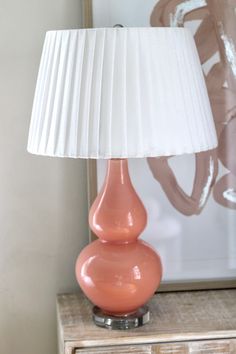 a pink lamp sitting on top of a wooden table next to a white shade covering