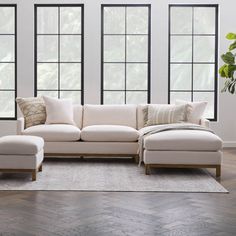 a living room scene with focus on the sectional sofa and footstool in front of three windows