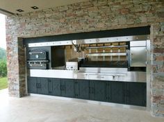 an outdoor kitchen with stone walls and stainless steel appliances