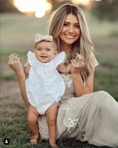 a woman holding a baby wearing a white dress and smiling at the camera with her hands in the air