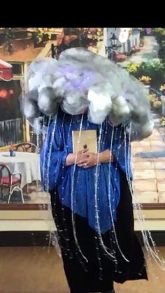 a woman is dressed up as a cloud with chains on her head and holding a book