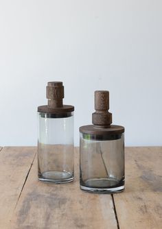 two glass jars sitting on top of a wooden table next to each other, one with a brown lid