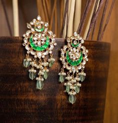 pair of green and white chandelier earrings sitting on top of a wooden stand