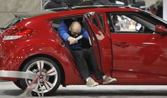 a man sitting in the driver's seat of a red car with his hand on the door handle