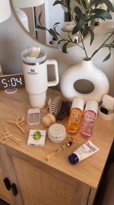 an assortment of personal care items sitting on a table next to a vase and mirror