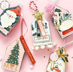 four christmas tags are hanging on a pink background with other ornaments and decorations around them