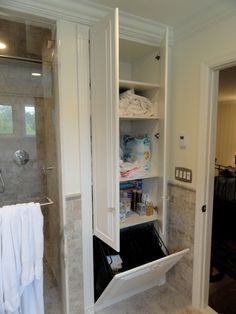 an open cabinet in a bathroom with towels hanging on the wall