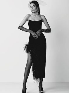 a woman in a black dress with feathers on her head and legs, standing against a white background