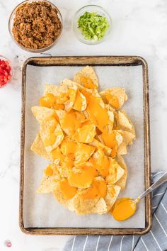 nachos with cheese and salsa on a tray next to bowls of condiments