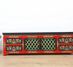 an ornately decorated red and black sideboard with floral designs on the doors, in front of a potted plant