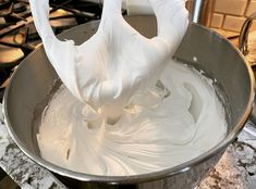 a metal bowl filled with white frosting on top of a stove