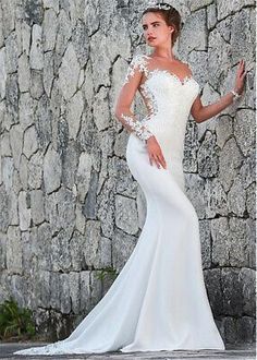 a woman in a white wedding dress standing next to a stone wall with her hand on her hip