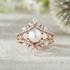 a close up view of a ring with pearls and diamonds on the bottom, in front of a pine tree