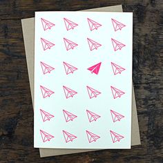 a card with pink origami paper airplanes on it, sitting on a wooden surface