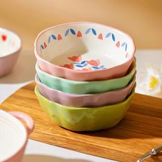 four bowls stacked on top of each other with spoons next to them and flowers in the background