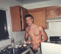 a shirtless man standing in a kitchen next to a sink