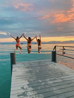 three women jumping into the water from a dock at sunset with their arms in the air