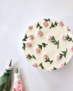 a cake decorated with pink roses and green leaves on top of a white table next to a pair of scissors